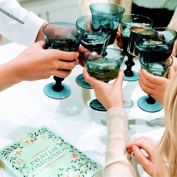Group of women referring to Catholic All Year Prayer Companion book and cheering their glasses together
